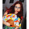 young woman with long red hair and blue glasses holds the multicolored fan looking at the camera smiling