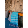 a turquoise hammam towel on the back of an outdoor sofa with two large black and white striped pillows