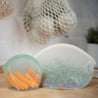 big and small silicone pouch huggers with salad and carrots inside on a kitchen table 